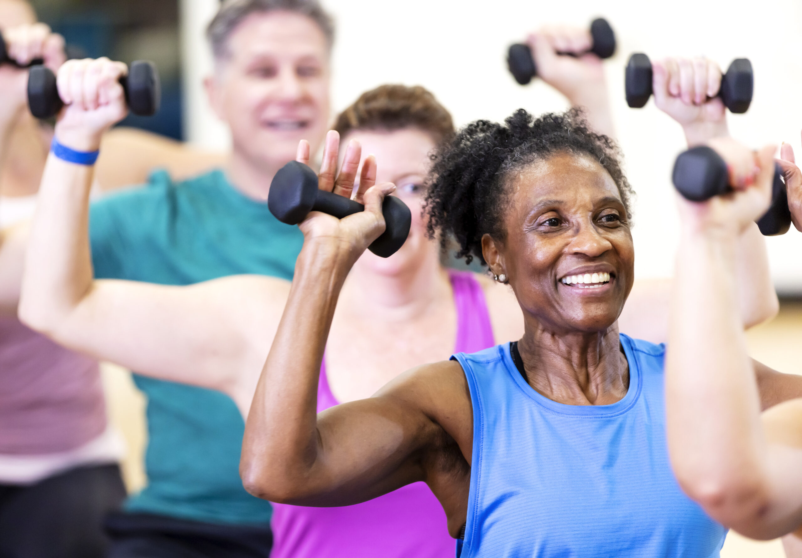 Close-up of a senior African-American woman in her 60s enjoying an exercise class. She is with a multiracial group of mature adults sitting on fitness balls and lifting hand weights.